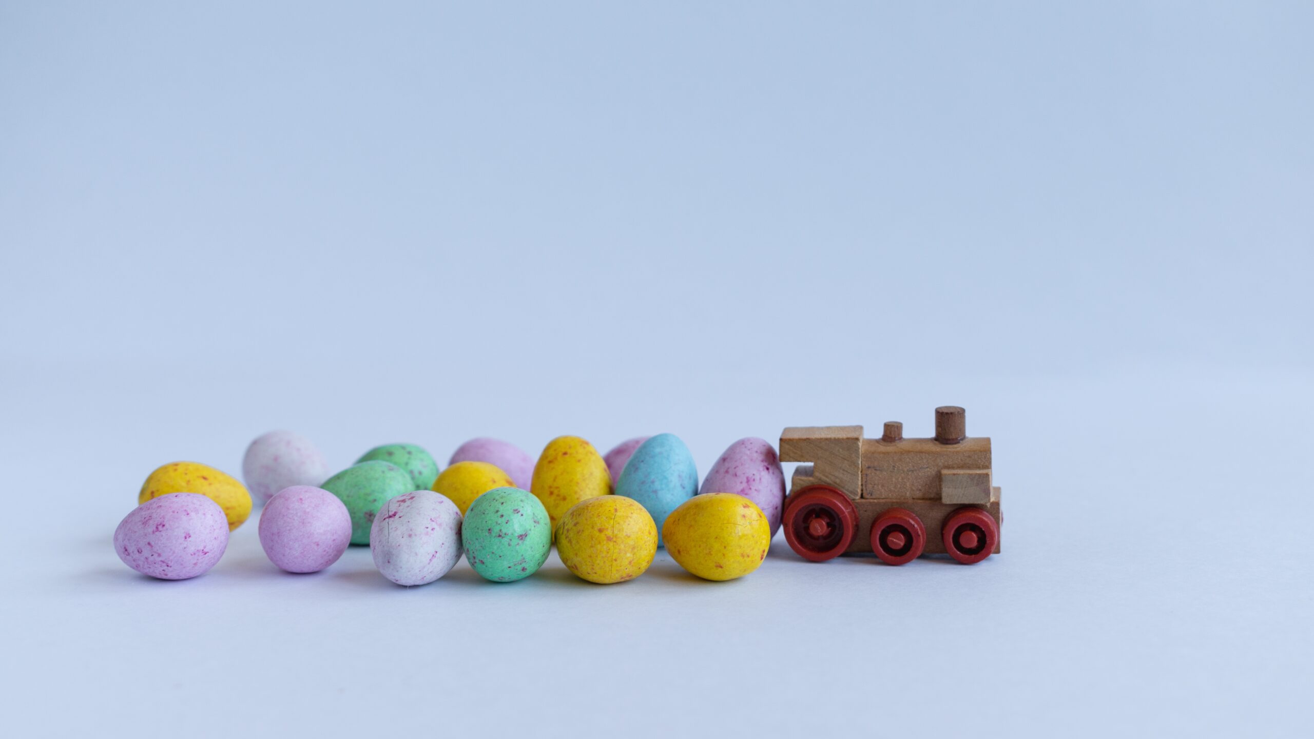 Wooden toy train with multicoloured easter eggs trailing behind it.