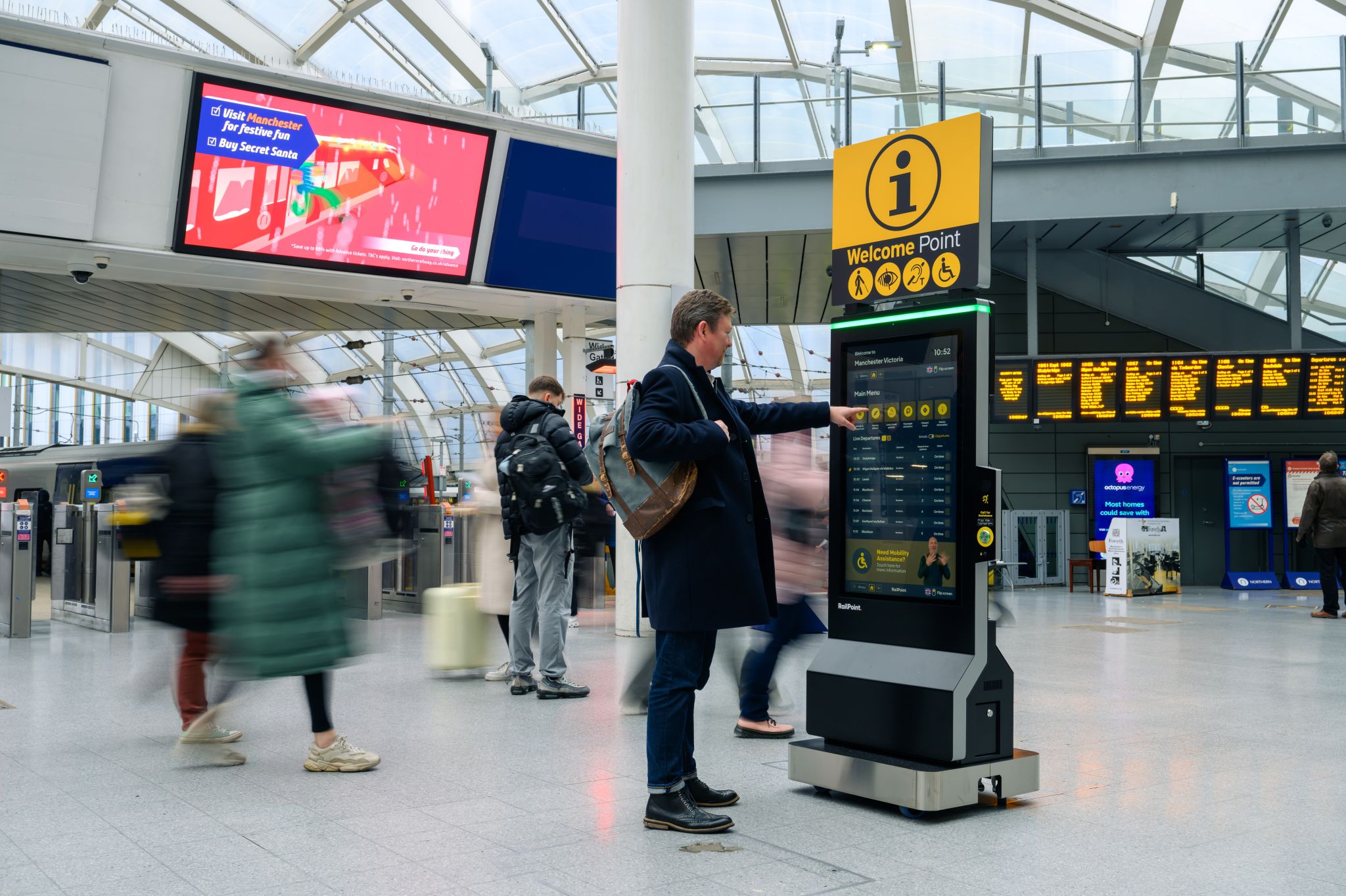 A passenger using a Welcome Point at a train station. The Welcome point is tall with a black letter 'i' on a yellow background at the very top so it is easily visible