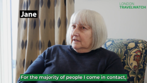 Still from London TravelWatch's 2023 video speaking to digitally excluded Londoners. The image shows an elderly lady seated in doors and speaking to someone off camera. She had shoulder length white hair and is wearing a navy blue jumper.