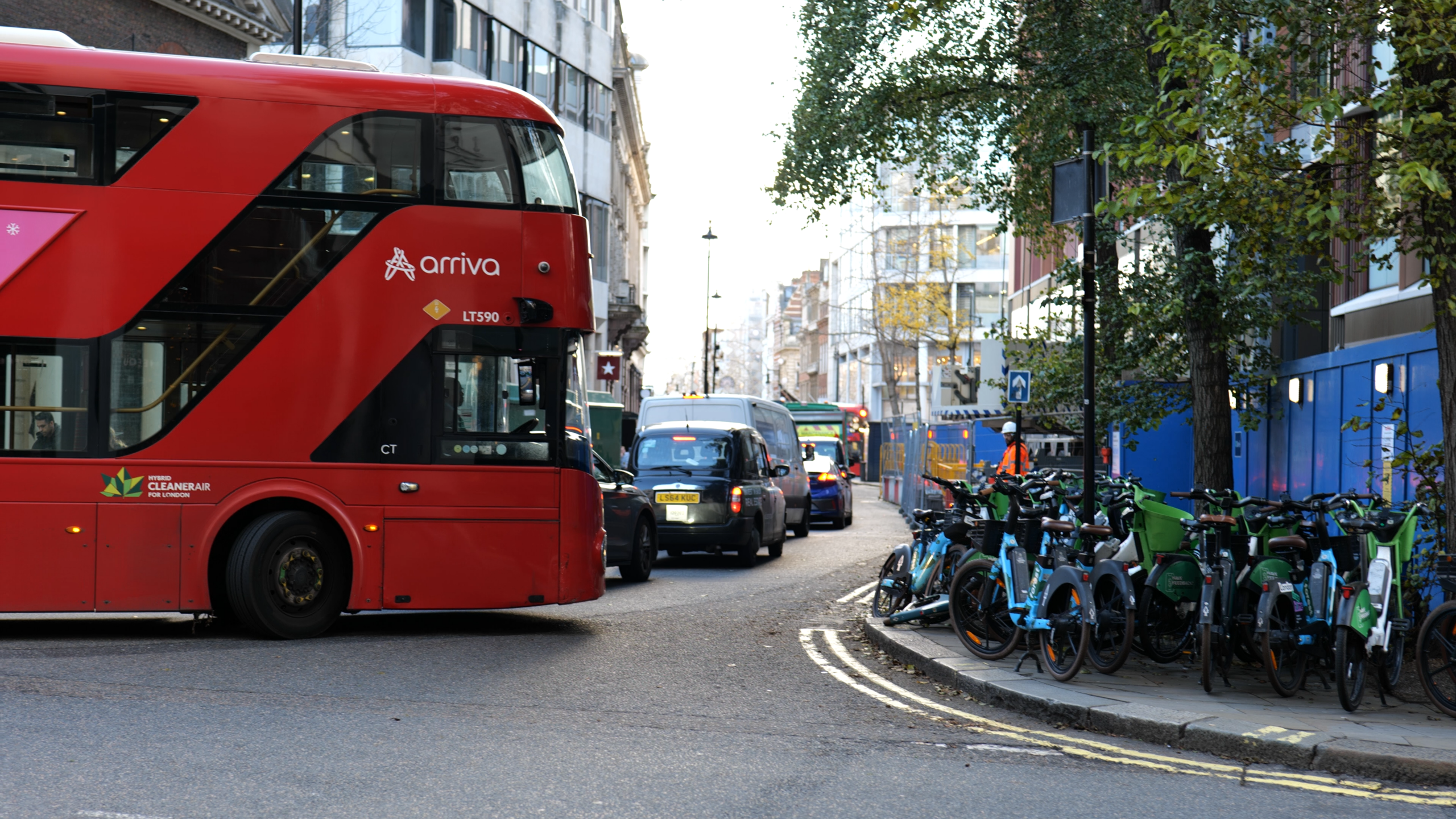 A red London bus turning a corner behind a row of traffic